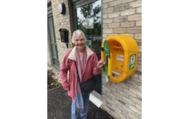 A female member of Kildrum Comminuty Council unveiling the new defibrilllator and smiling
