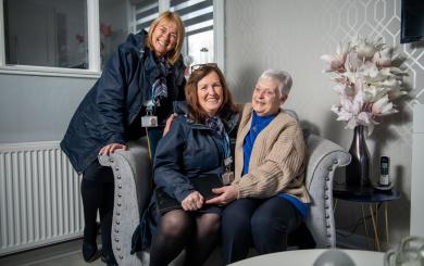 Two Sanctuary staff members with a female resident in her living room
