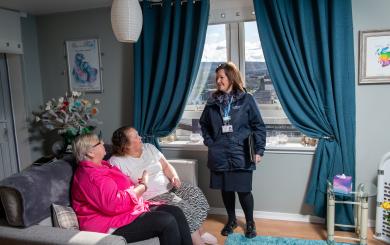 Two female residents sat on the sofa in their home with a Housing Officer chatting to them