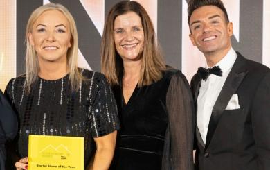 Three people dressed in formal attire at an awards event. The person on the left is holding a yellow award plaque that reads 'Scottish Home Awards 2023 - Starter Home of the Year