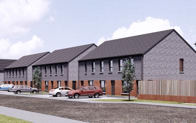 "Row of modern two-story suburban houses with dark gray and red brickwork, pitched roofs, and multiple windows. Cars are parked along the street, and small trees line the grassy area between the sidewalk and road. A wooden fence encloses part of one property under a partly cloudy sky.