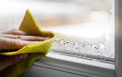 Hand wiping condensation from a window, showing early signs of damp.