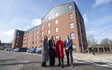 From left to right - Pat Cahill Director of Housing and Property at Sanctuary Scotland, Màiri McAllan Scottish Housing Secretary, Gill Lavety Development Director for Sanctuary Scotland, David Wylie, Managing Director, CCG Scotland. They stand infront of Adam Place a 5 story block of apartments made of brick with black panelling on the walls of the top floor.