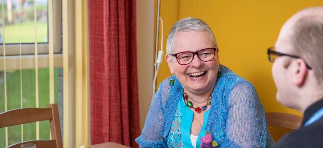 Sanctuary Scotland resident sitting in their living room and smiling with a housing officer