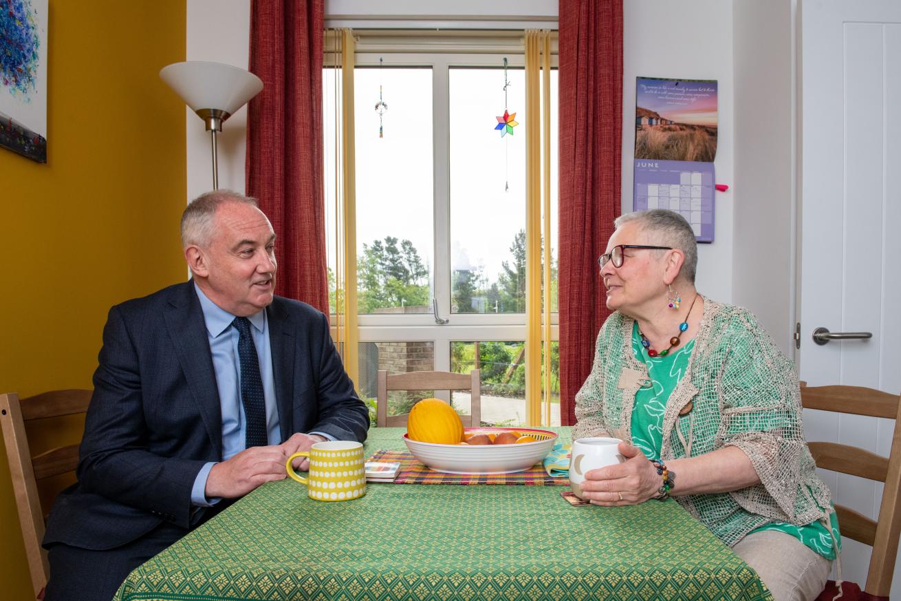 Two people sitting at a kitchen table and talking with cups of tea