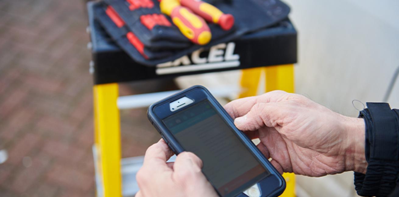 A close up of somebody using an app on a mobile phone with a set of tools on a step ladder in the background