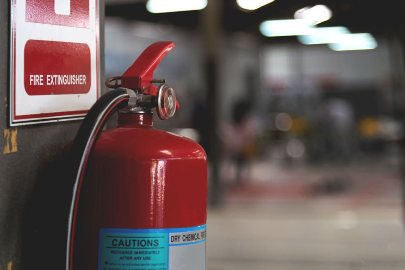 A red fire extinguisher hanging on a black wall underneath a fire safety sign