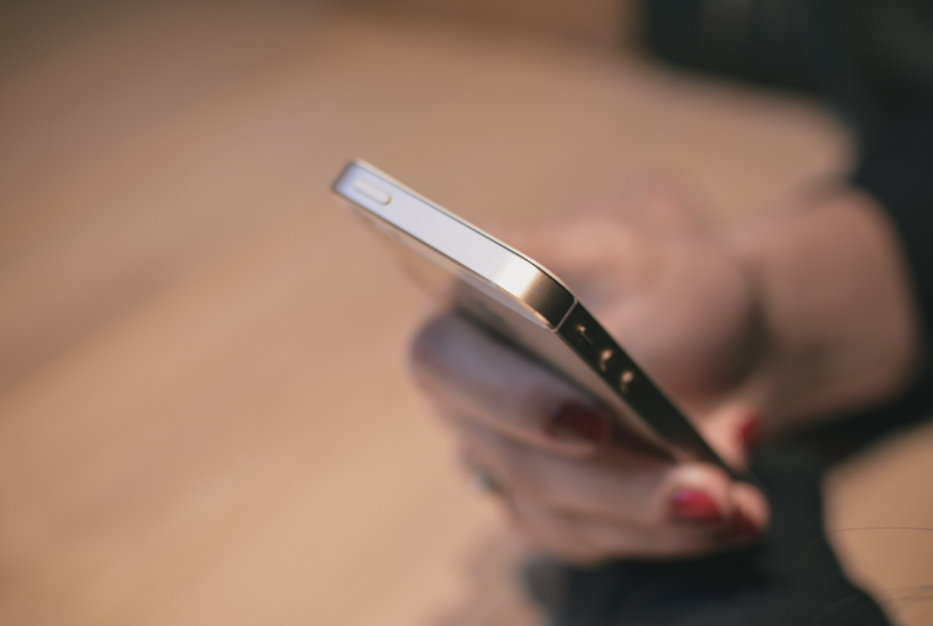 A female hand with red nail polish holding an IPhone