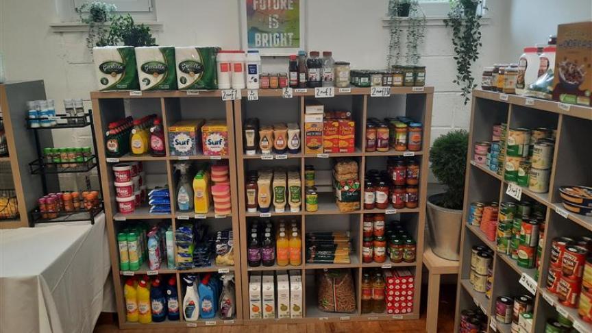 A collection of supermarket items including canned goods, sauces, dried goods and cleaning supplies stacked on wooden shelves