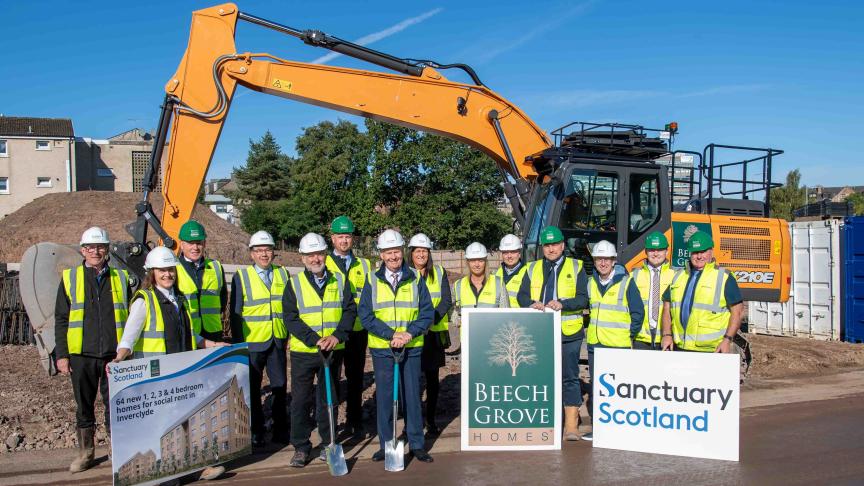 A group of 14 people wearing high vis and hard hats stood in front of a housing development site on a sunny day