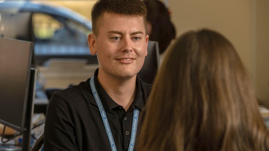 Sanctuary Scotland employee wearing a black polo top and Sanctuary Scotland lanyard talking to a colleague