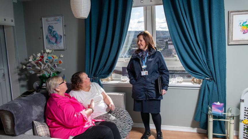 Two female residents sat on the sofa in their home with a Housing Officer chatting to them