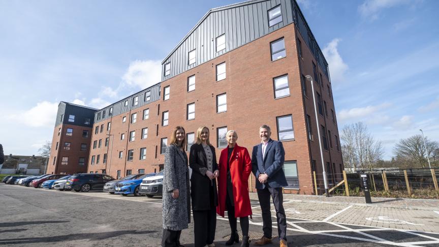From left to right - Pat Cahill Director of Housing and Property at Sanctuary Scotland, Màiri McAllan Scottish Housing Secretary, Gill Lavety Development Director for Sanctuary Scotland, David Wylie, Managing Director, CCG Scotland. They stand infront of Adam Place a 5 story block of apartments made of brick with black panelling on the walls of the top floor.