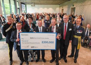 A large group of people standing in a room raising their glasses in celebration. In the forefront of the picture are six males and one female holding a large cheque for £200,000 from Sanctuary to the Armed Forces charity. Some of the men are wearing military medals.