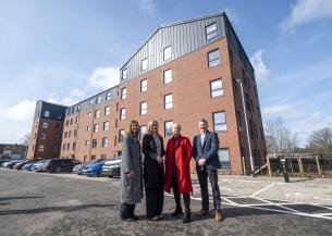 From left to right - Pat Cahill Director of Housing and Property at Sanctuary Scotland, Màiri McAllan Scottish Housing Secretary, Gill Lavety Development Director for Sanctuary Scotland, David Wylie, Managing Director, CCG Scotland. They stand infront of Adam Place a 5 story block of apartments made of brick with black panelling on the walls of the top floor.