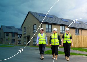 Three people wearing high-visibility clothing and hard hats walking through a residential housing development with solar panels on the roofs.